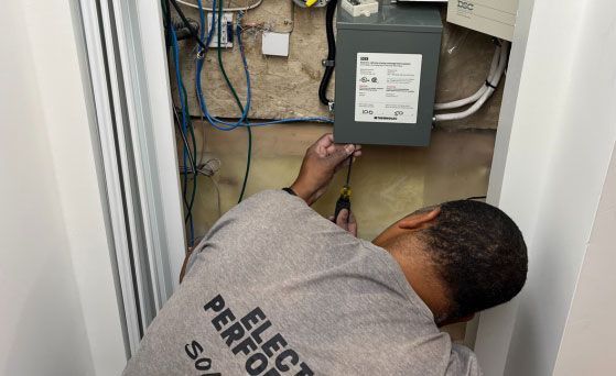 Person working on electrical panel in a recessed wall. Wires visible. Gray panel and wiring.