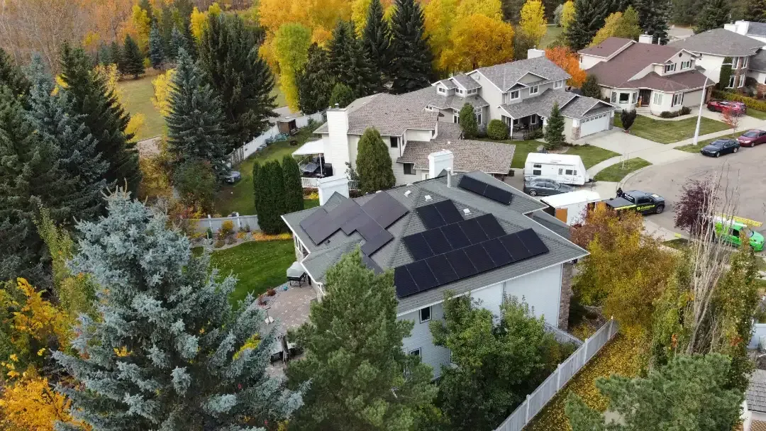 Aerial view of a house with solar panels on the roof surrounded by trees with fall colors.