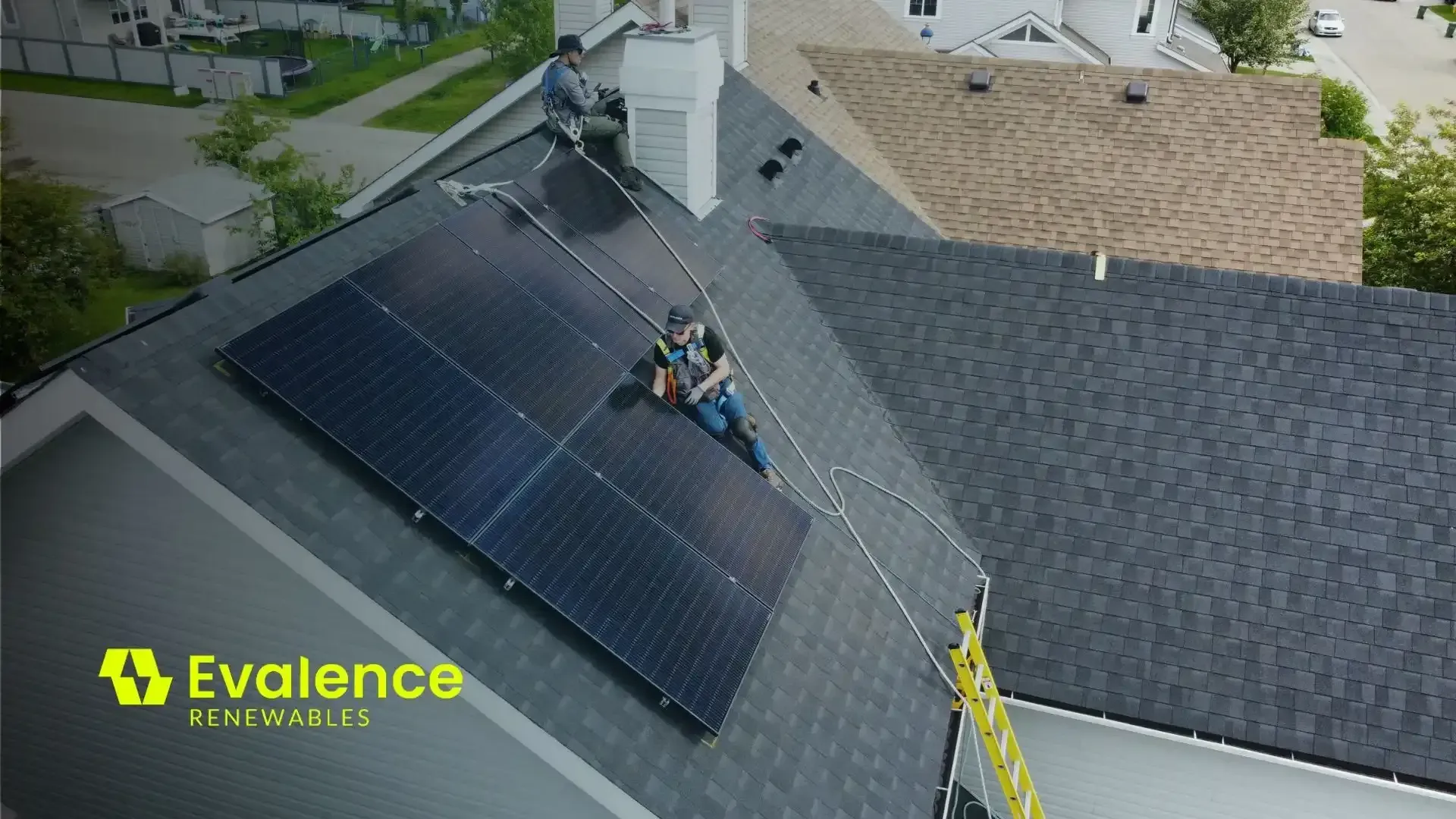 Workers installing solar panels on a residential roof, with a ladder and the Evalence logo.