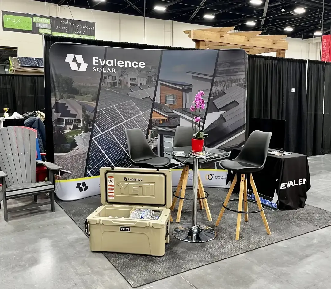 Trade show booth for Evalence Solar with a backdrop, seating, a cooler, and a small table.