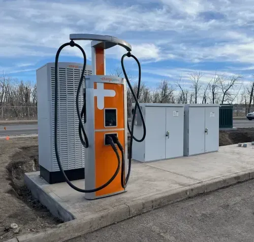 Orange and gray electric vehicle charging station with two cables, outdoors.