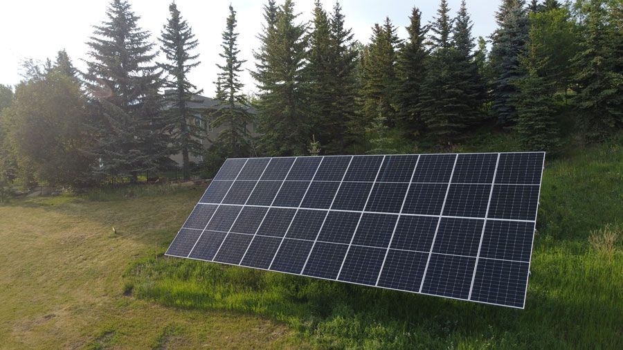 Solar panels on a grassy hill, with a backdrop of trees and a blue sky.