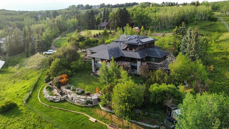 Large stone house on a green hillside with trees and a winding road.