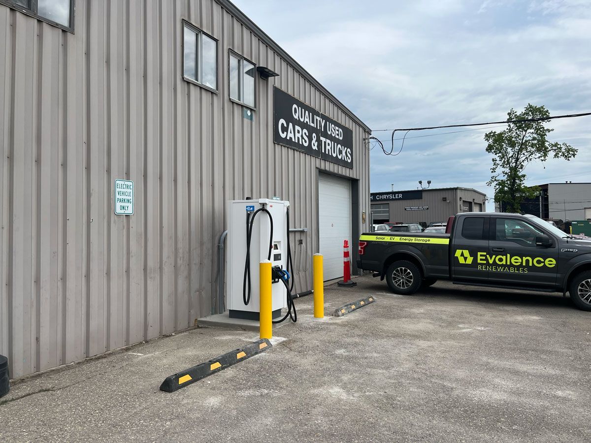 Exterior of a building with an EV charger next to the entrance. A black Evalence truck is parked nearby.