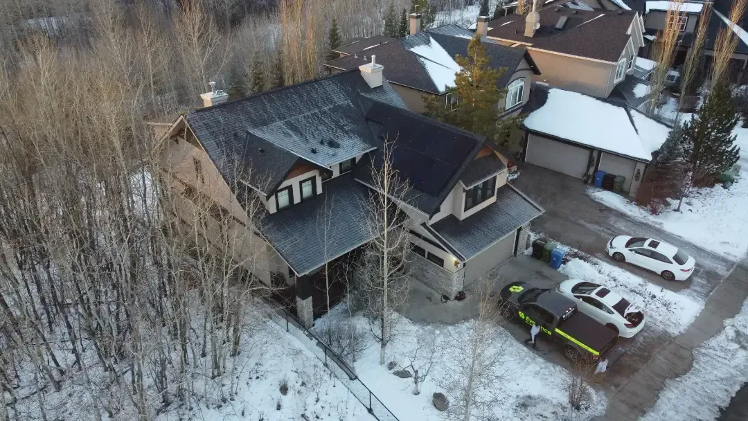 Aerial view of a two-story house with a driveway. Cars parked on snow-covered ground.