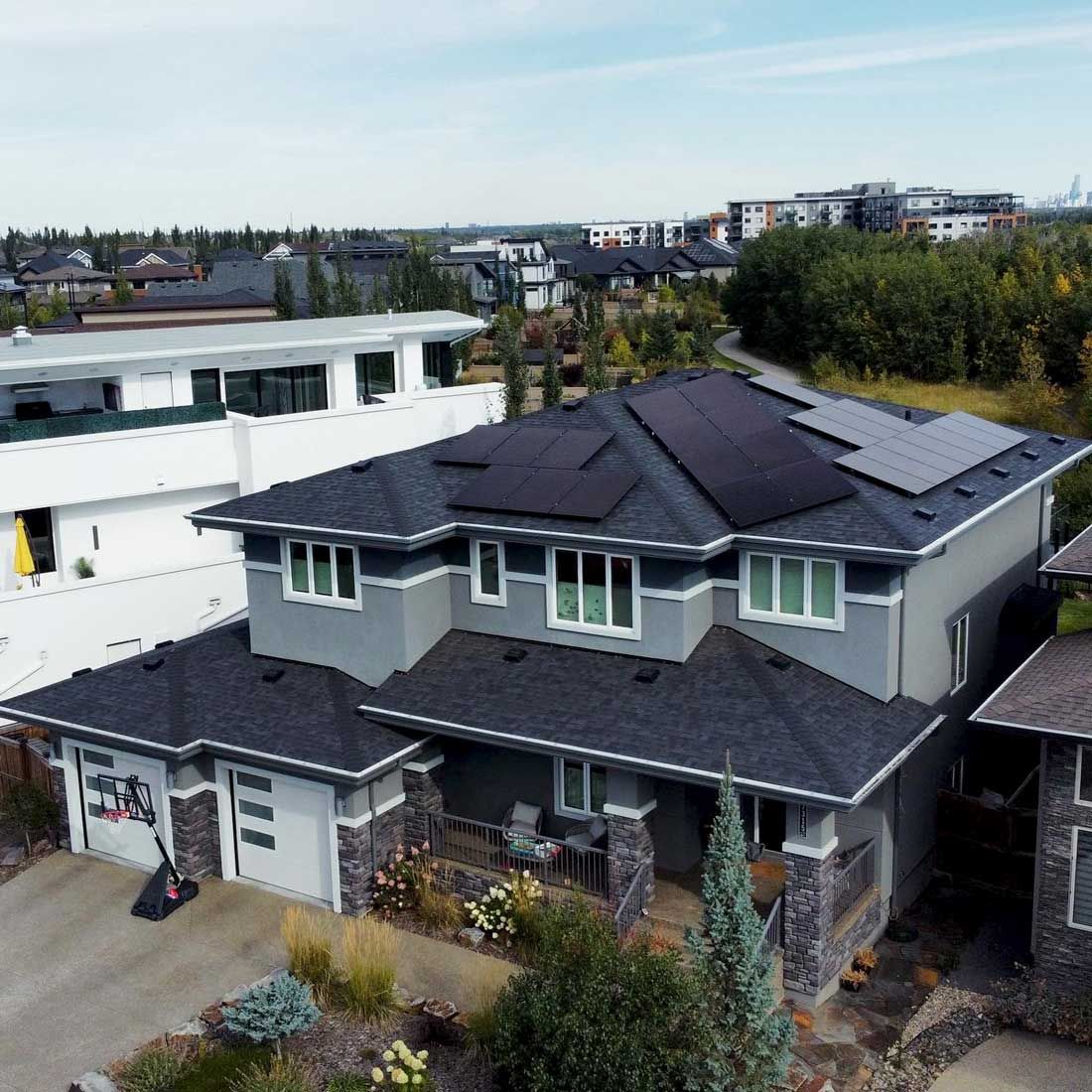 A two-story house with solar panels on the roof. Gray siding, multiple windows, and a green yard.