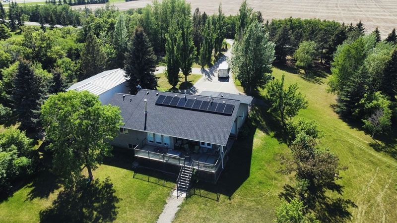Aerial view of a house with solar panels on the roof, surrounded by trees and a long driveway.
