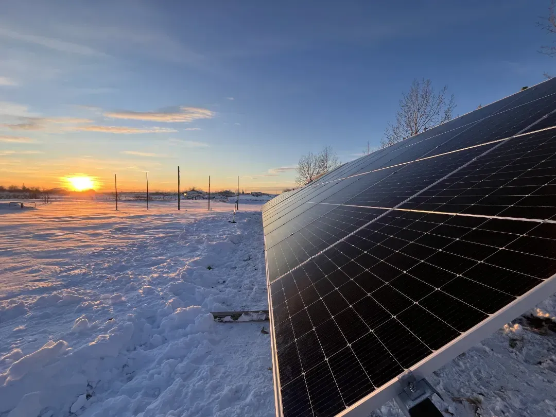 Solar panel in a snowy field at sunset. Blue sky, orange sun, frost on the panel.
