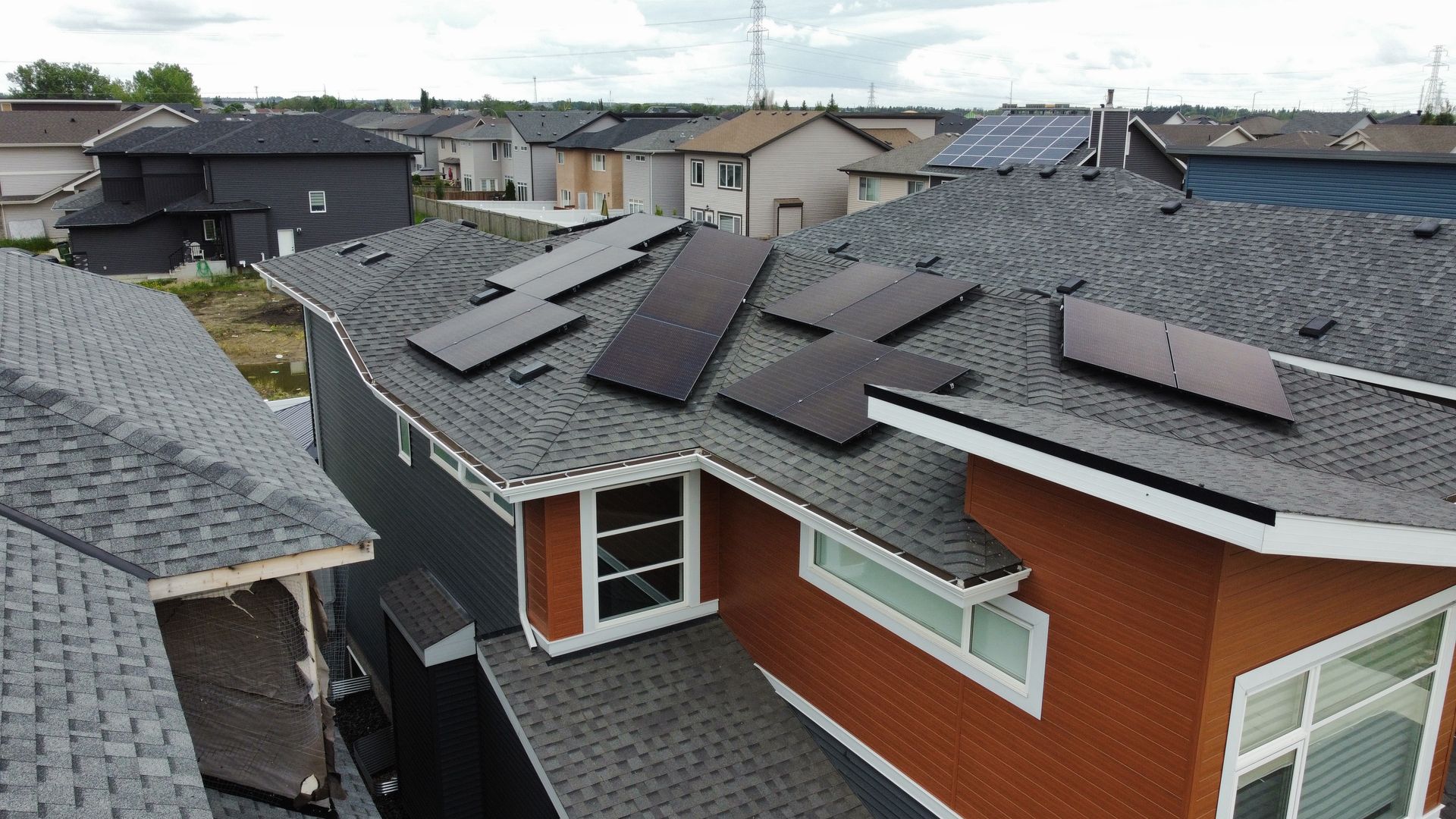Rooftop solar panels on the roof of orange and grey house. Grey shingles, dark panels. afternoon scene.