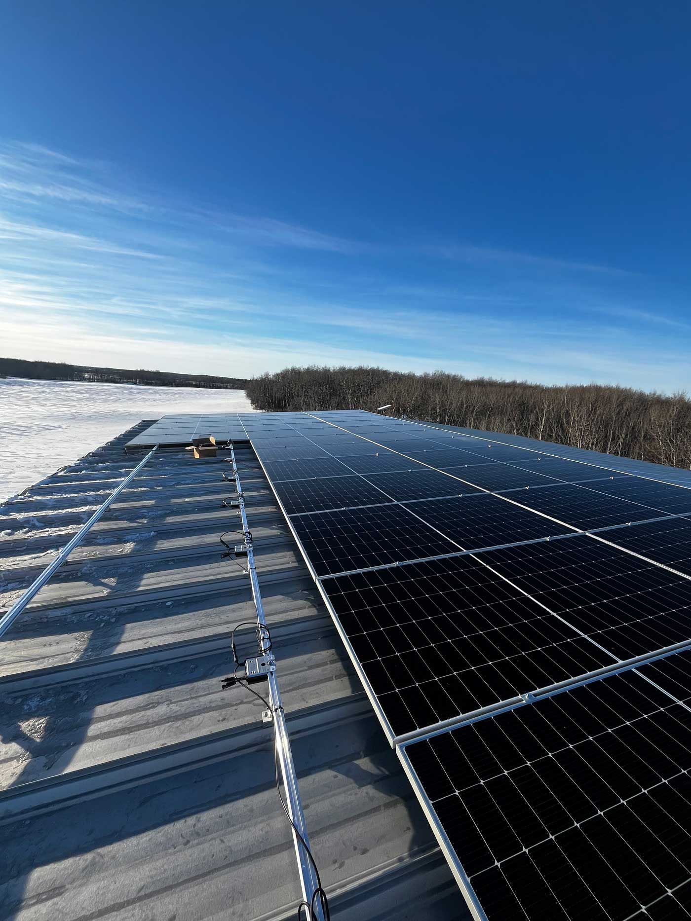 Solar panels on a snowy metal roof under a bright blue sky.