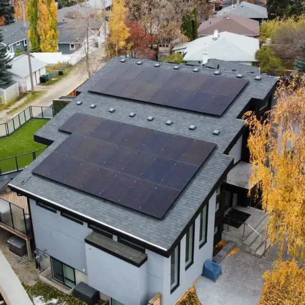 Aerial view of a house with solar panels on its dark gray roof. Autumn trees surround the house.