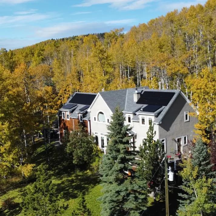 House with solar panels on roof surrounded by trees with yellow autumn leaves under a blue sky.