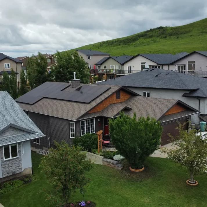 Houses with solar panels on rooftops in a residential neighborhood, green hill in the background.