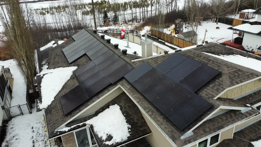 Building with solar panels on roof, open field, trees and mountains in background.