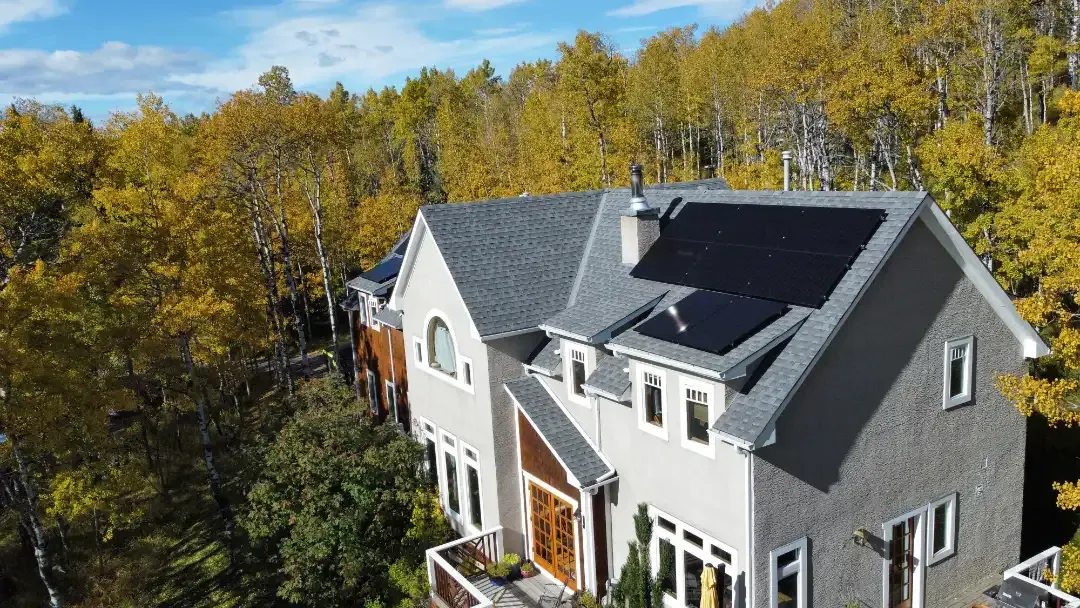 Two-story house with gray roof and solar panels, surrounded by trees with yellow and green leaves.