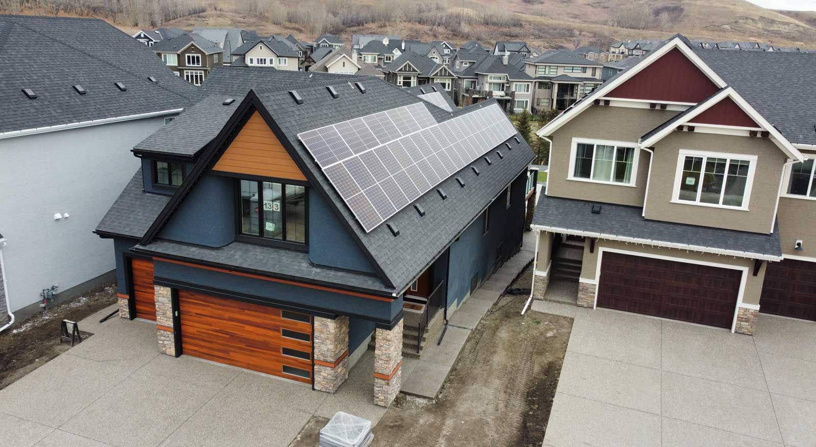 House with solar panels on roof, blue exterior, brown garage door, and houses in the background.