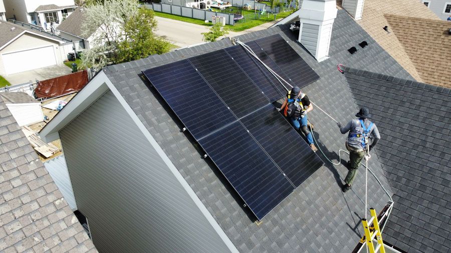 Two workers installing solar panels on a residential rooftop.