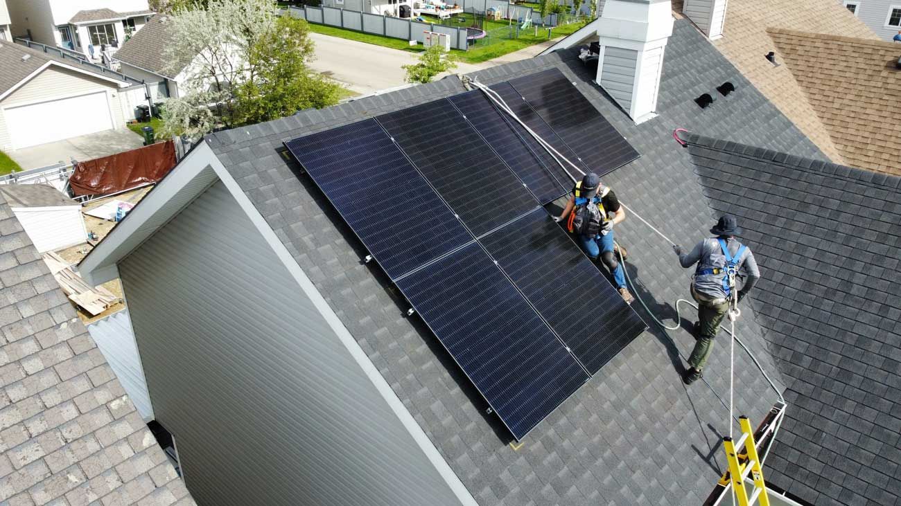 Workers installing solar panels on a residential roof, using safety harnesses.