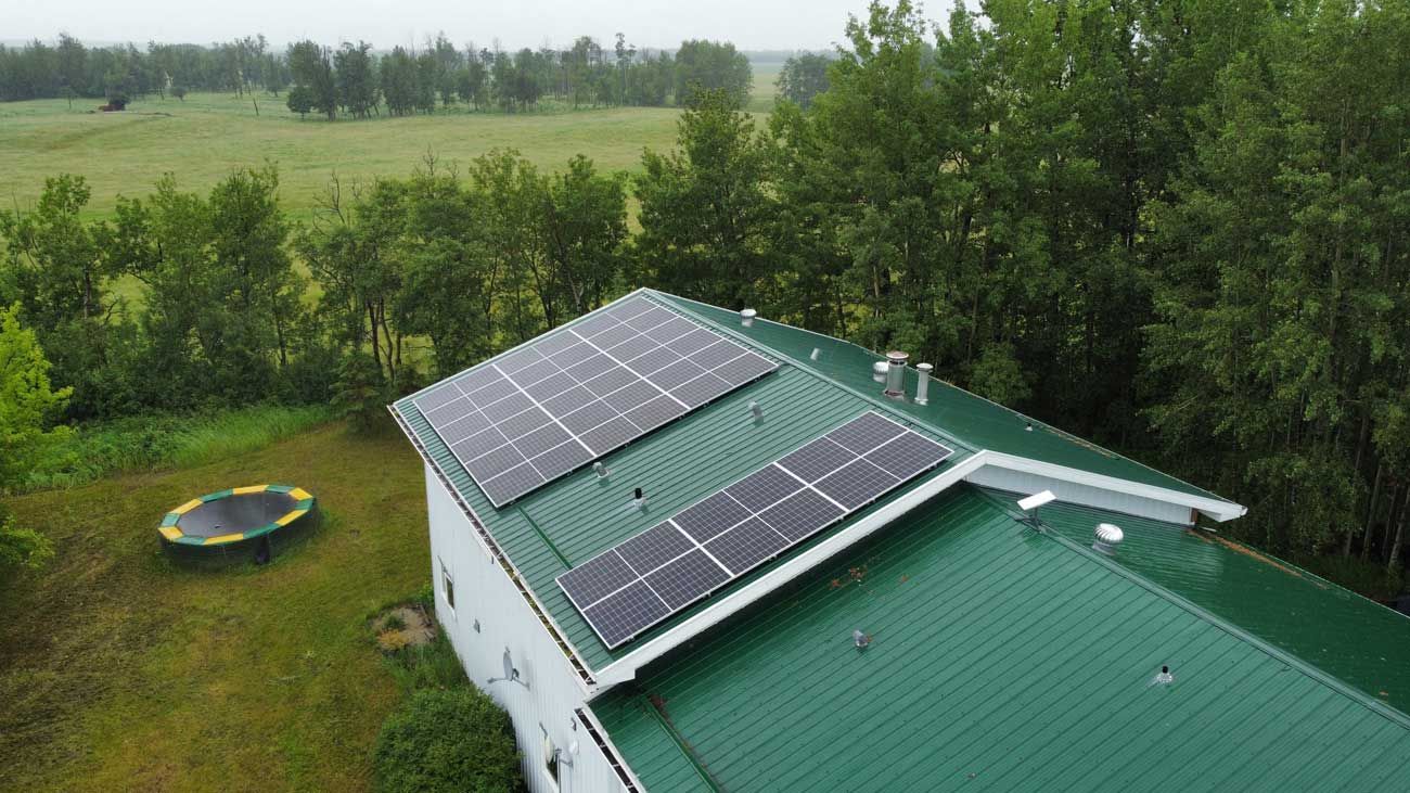 Solar panels on a green roof. A trampoline is on the lawn. Trees and fields are in the background.