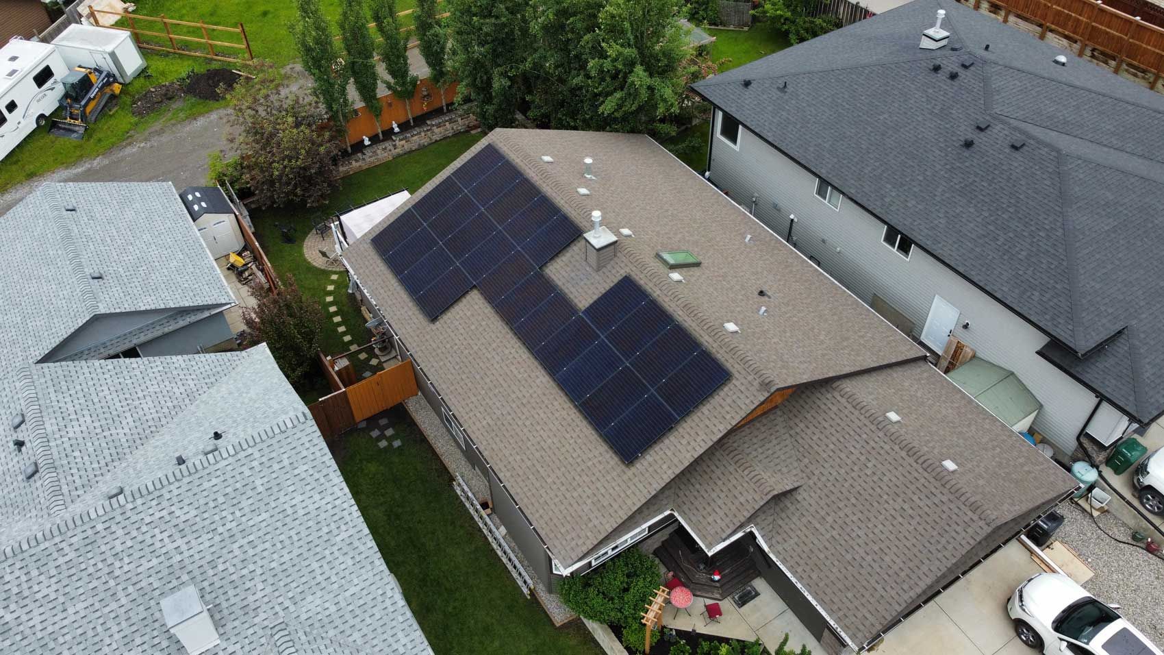 Aerial view of a house with solar panels on its roof, adjacent to other houses and a car parked in the driveway.