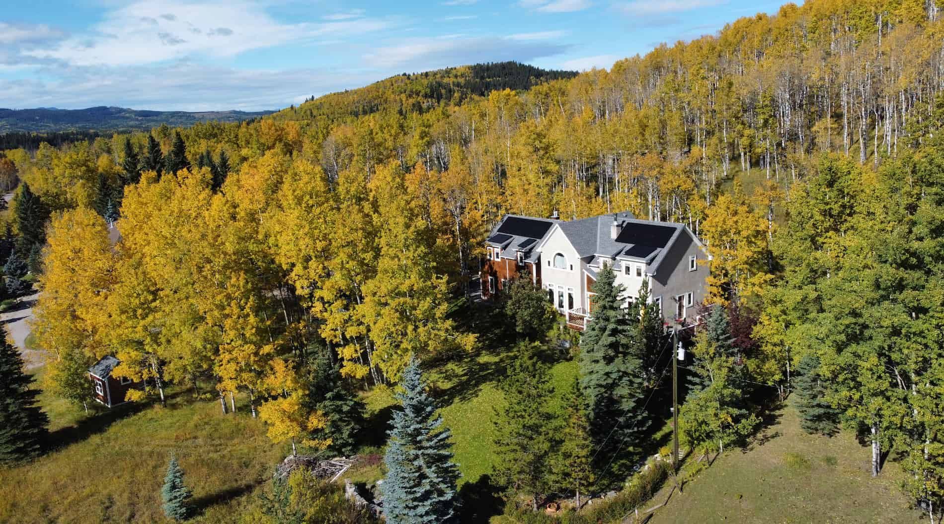 A house with solar panels installed nestled in a hillside of golden autumn trees, under a blue sky.