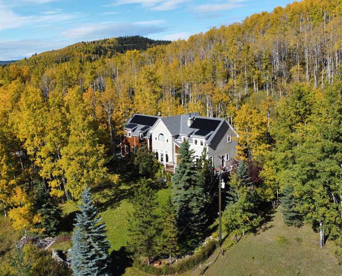 House surrounded by autumn trees, mostly yellow, on a hillside.