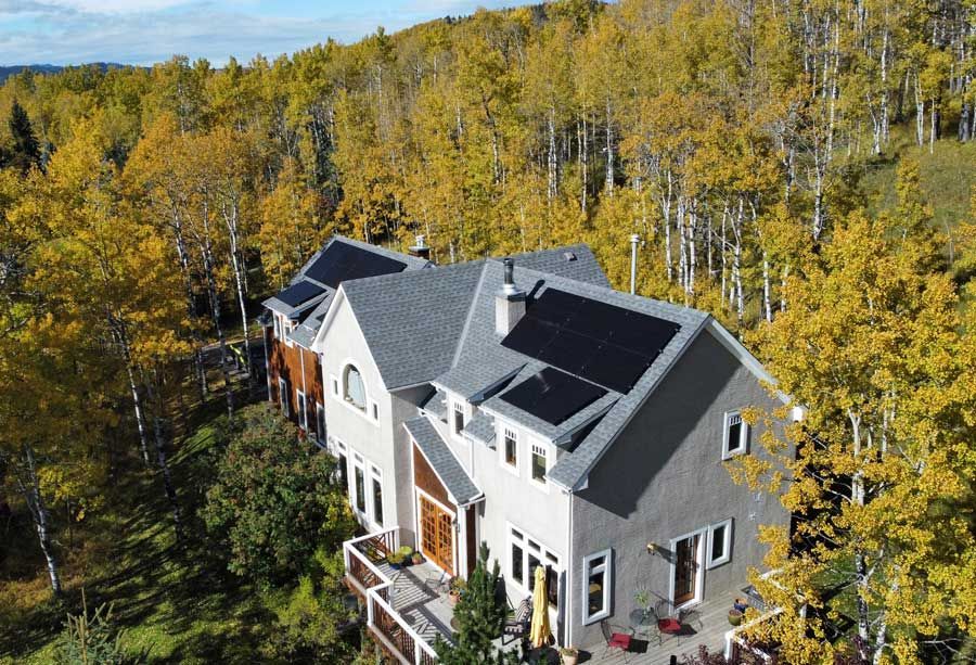 House with solar panels on roof surrounded by golden autumn trees.