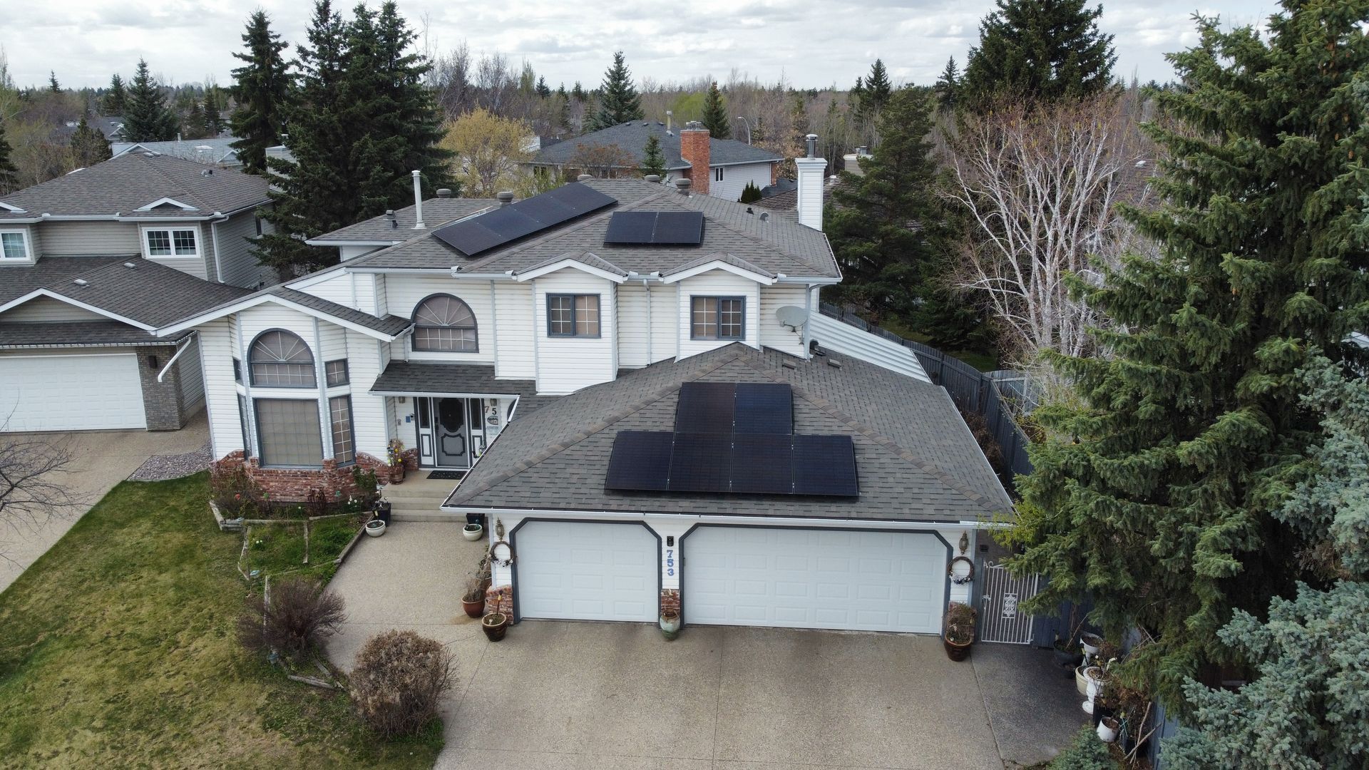 Two-story house with gray roof and solar panels, surrounded by some trees with and without leaves.