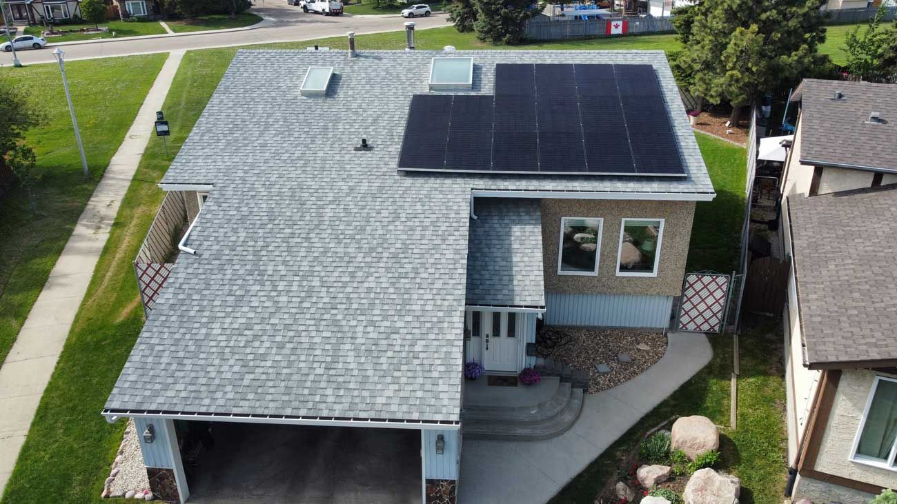 Aerial view of a house with solar panels on the roof. Gray roof, beige siding, green lawn.