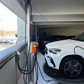 White Mercedes SUV charging at an outdoor station; snowy conditions.