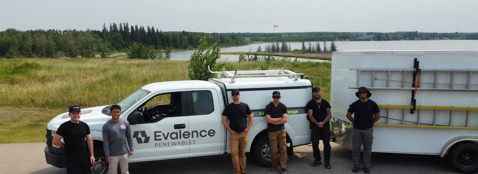 Group of employees by an Evalence Renewables truck and trailer with a natural landscape background.