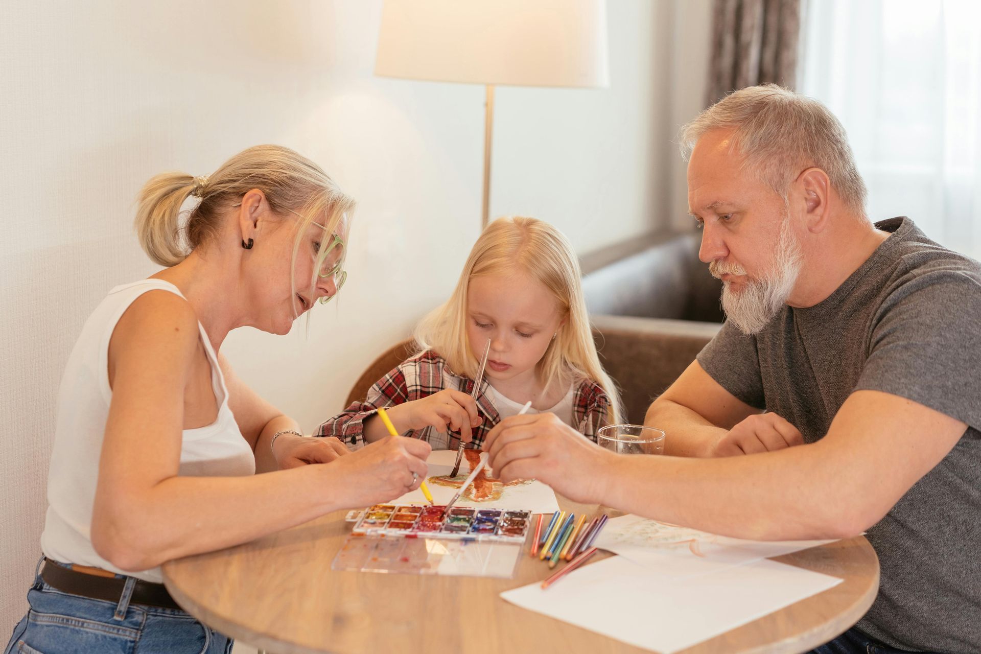 A child paints with grandparents at a table.