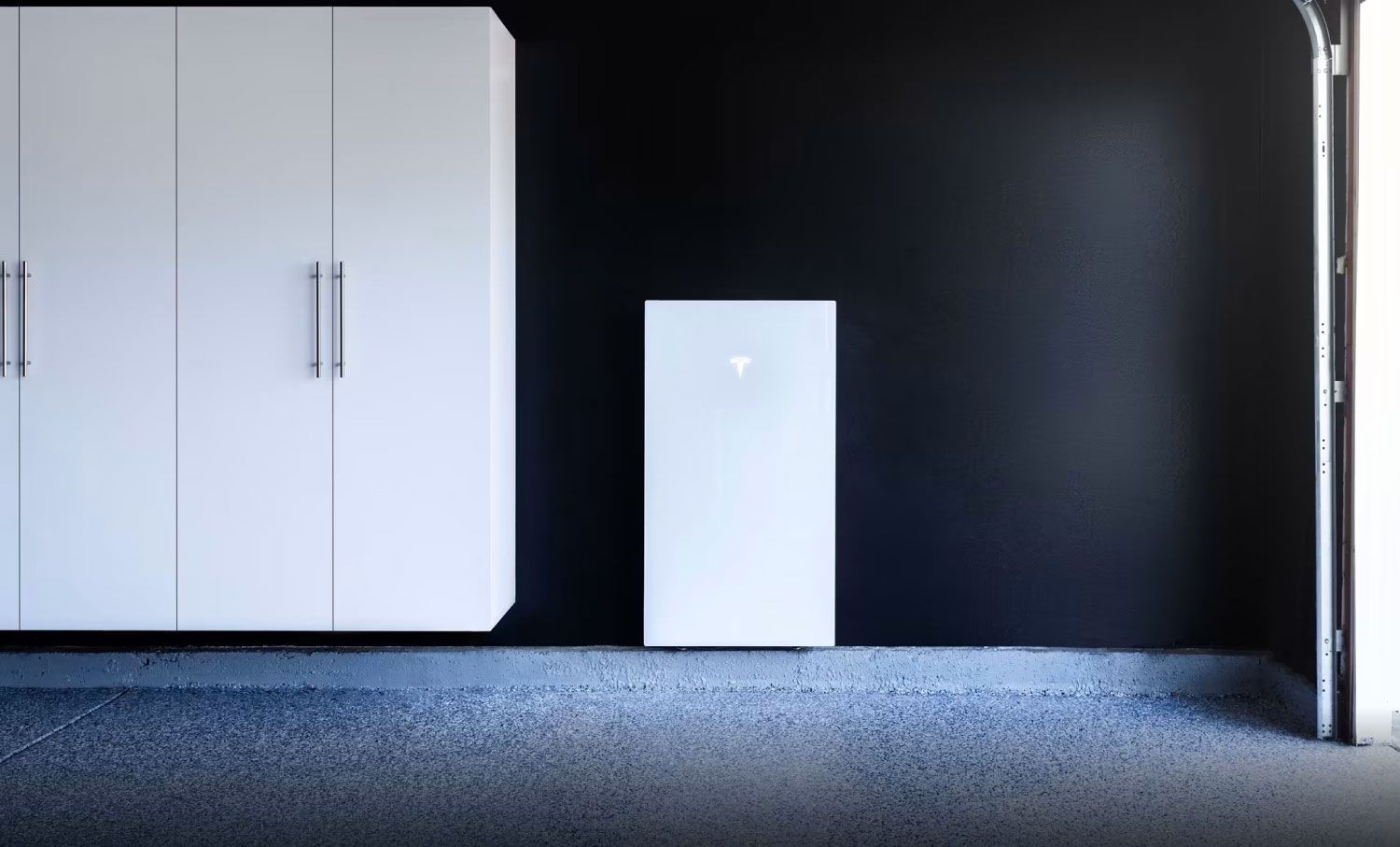 White Tesla Powerwall and storage cabinets in a garage with dark blue walls and a partly open garage door.