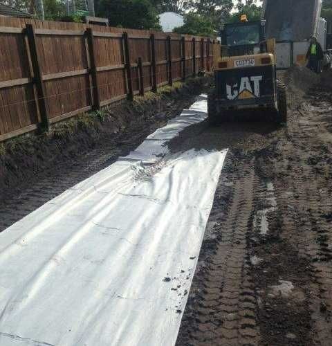 A cat Bulldozer is Driving down a dirt road next to a Wooden Fence — Roll Formed Driveways in Yandina, QLD