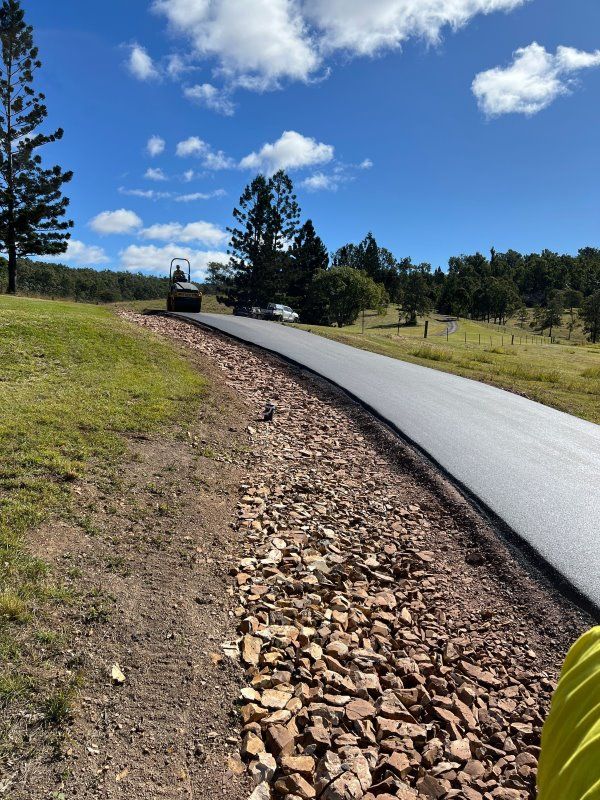 A Road That Is Going Through A Field With Trees On The Side Of It — Roll Formed Driveways in Yandina, QLD