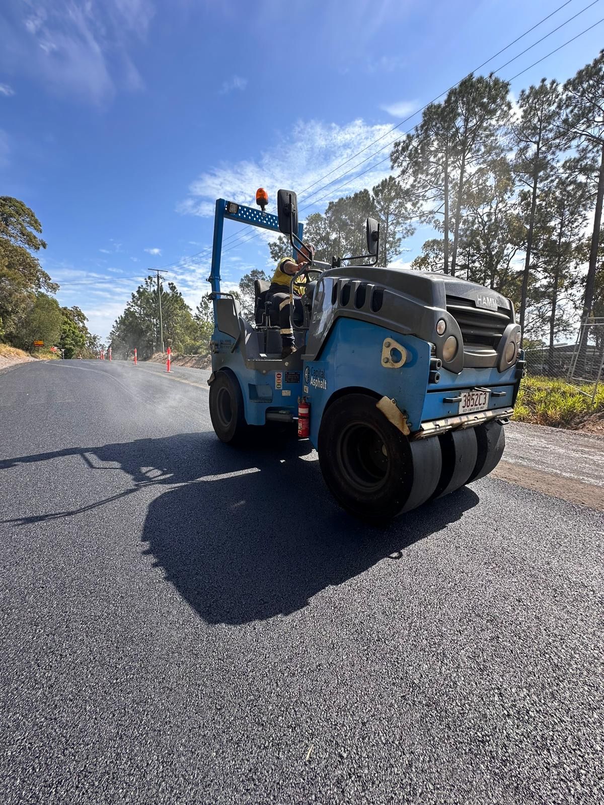 A Blue And Black Asphalt Roller Is Driving Down A Road — Roll Formed Driveways in Yandina, QLD