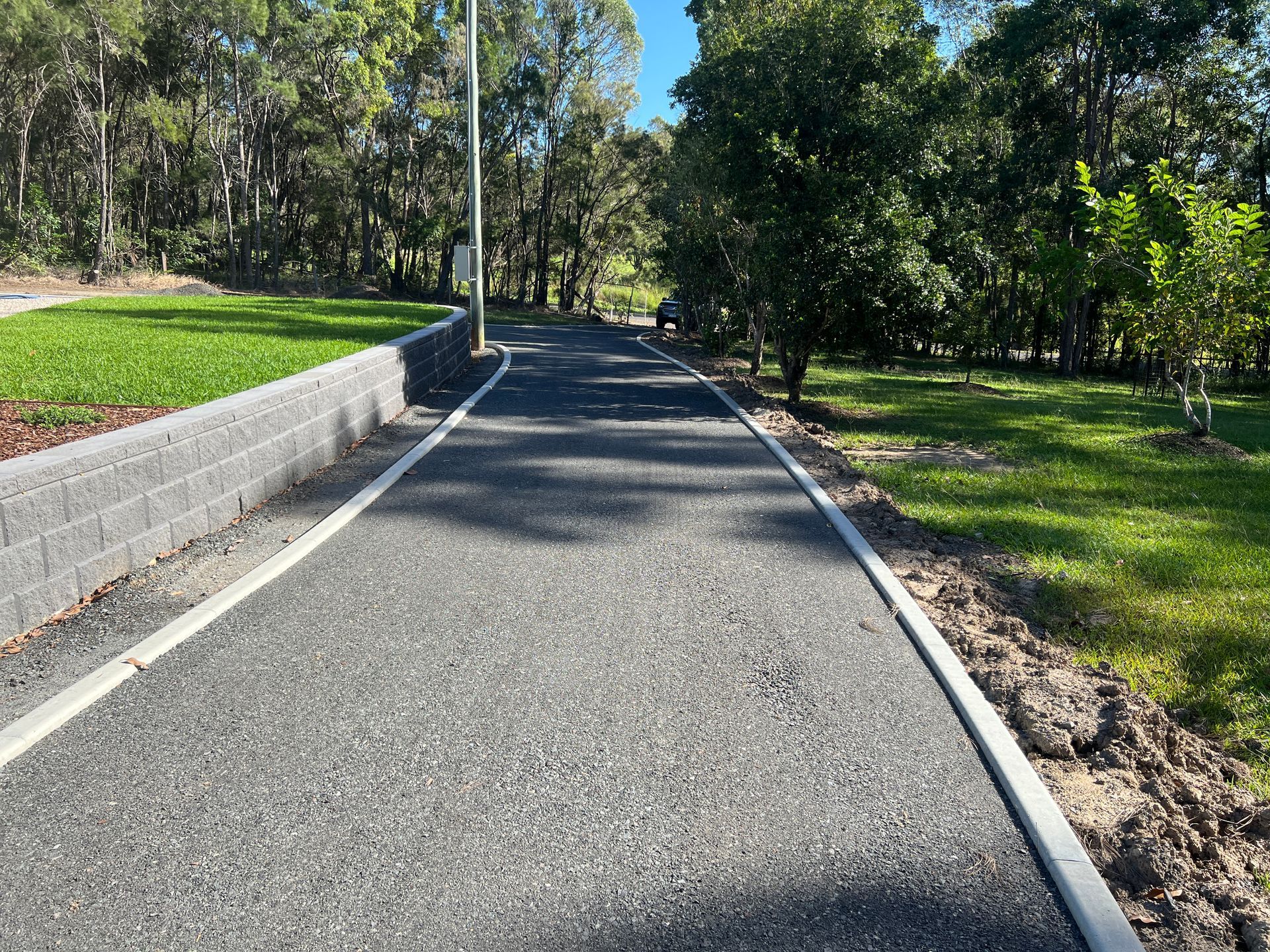 A gravel driveway is surrounded by trees and grass — Roll Formed Driveways in Yandina, QLD