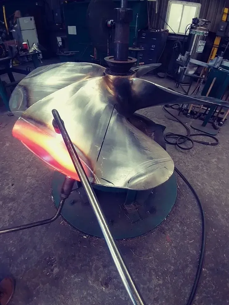 A large metal propeller is being worked on in a factory.