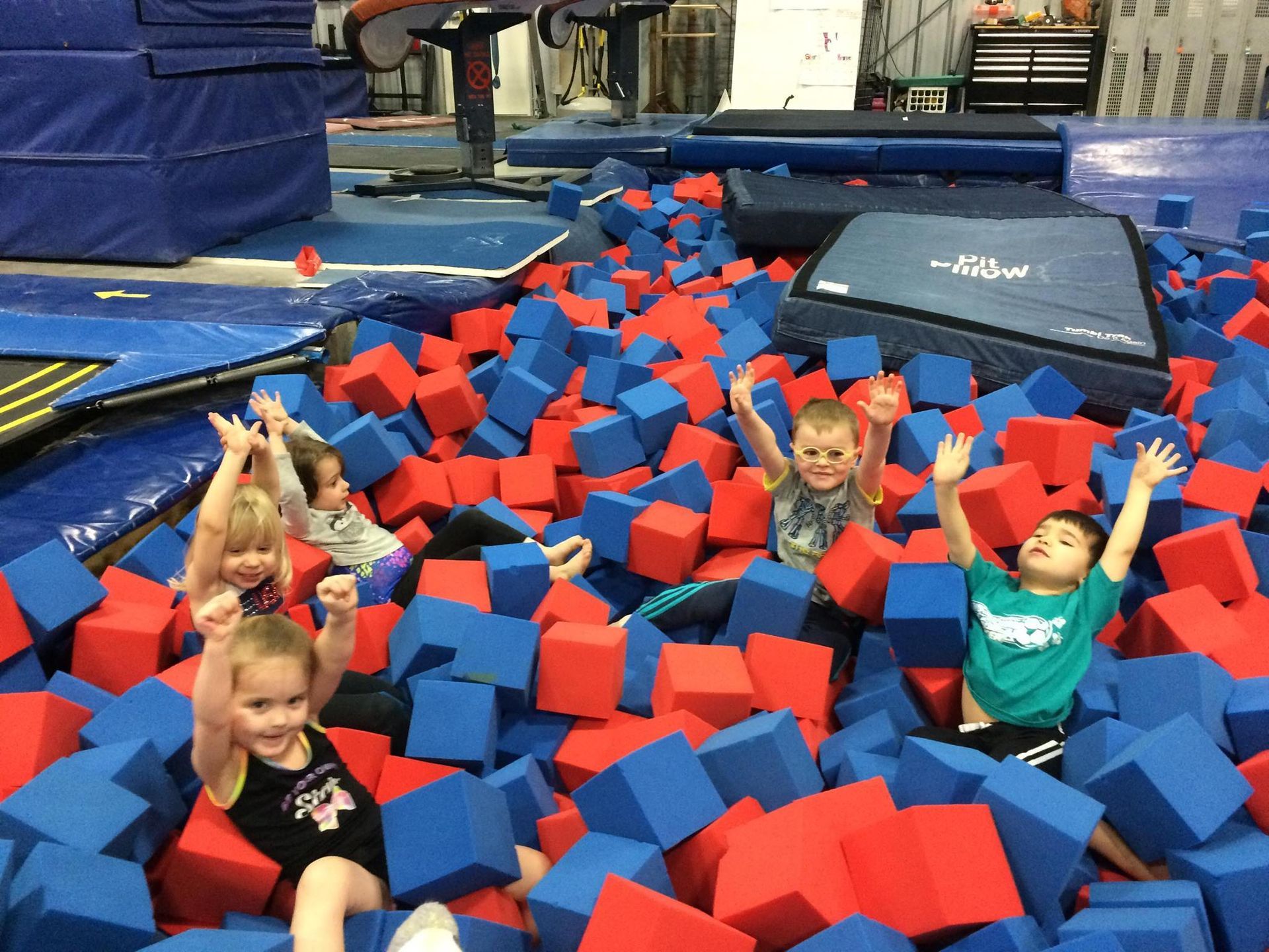 A group of children are sitting in a pile of foam cubes.