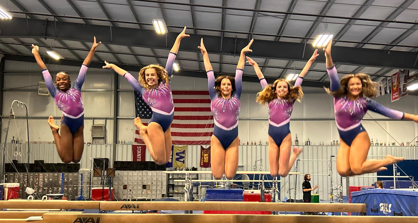 A group of female gymnasts are jumping in the air on a balance beam.