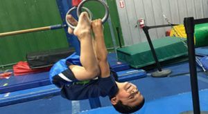 A young boy is doing a handstand on a pair of gymnastic rings.