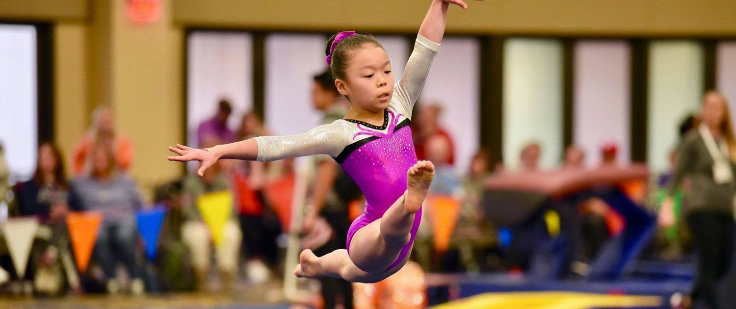 A young girl is doing a routine on a balance beam in a gym.