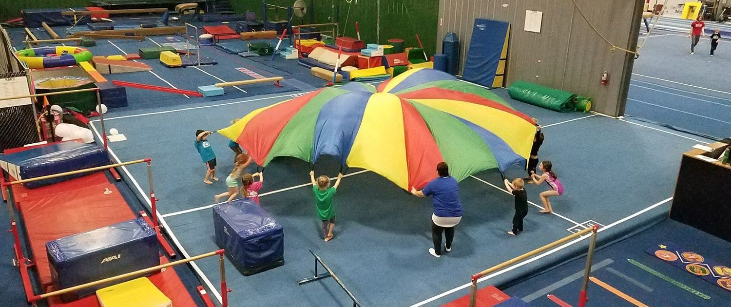 A group of children are playing with a colorful parachute in a gym.