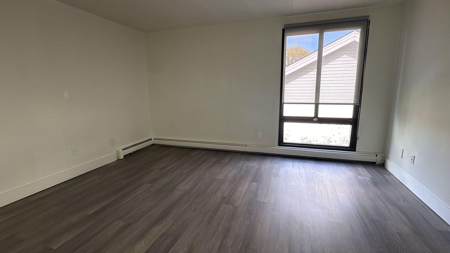An empty room with hardwood floors and a large window.