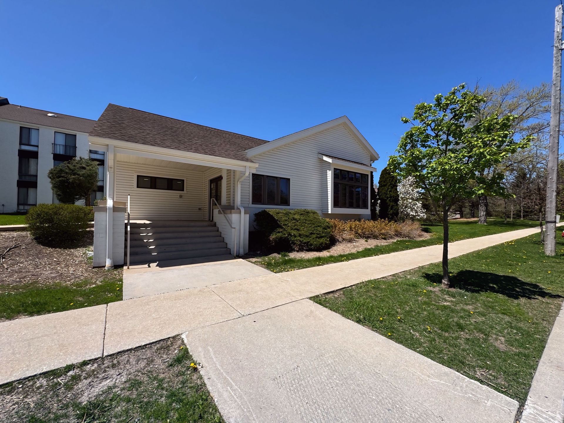 A white house with a walkway leading to it and a tree in front of it.
