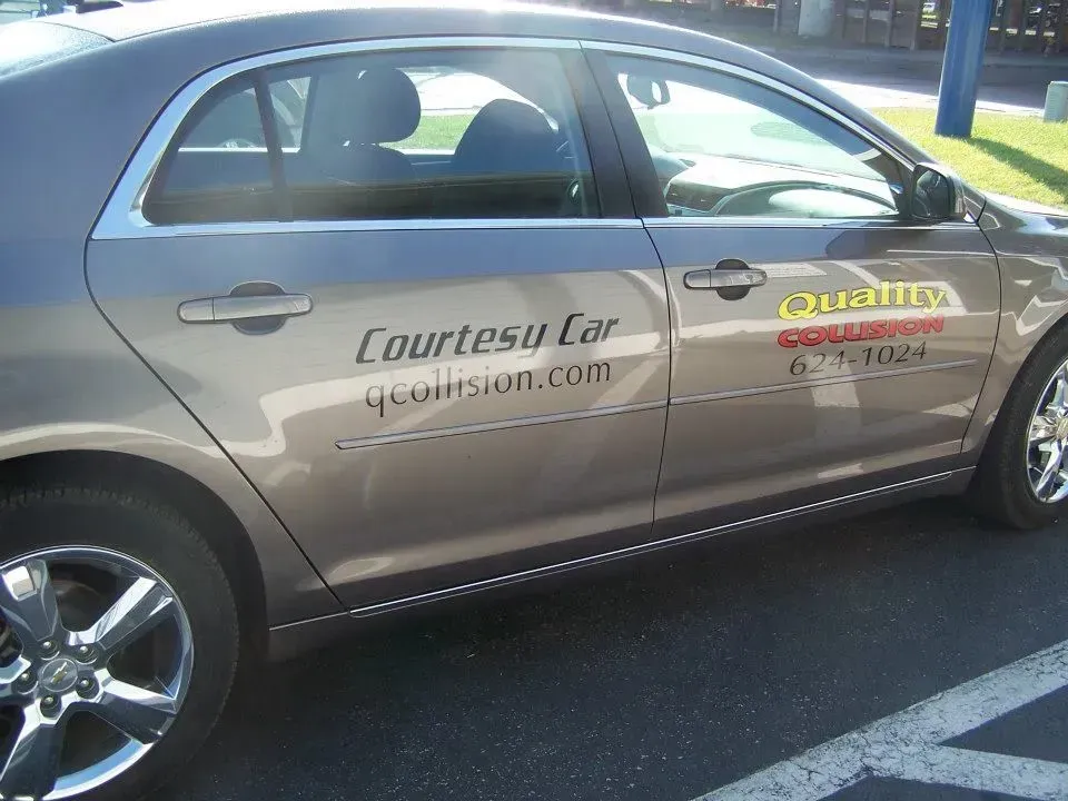Silver sedan with Courtesy Car and Quantum logo decals parked in a lot
