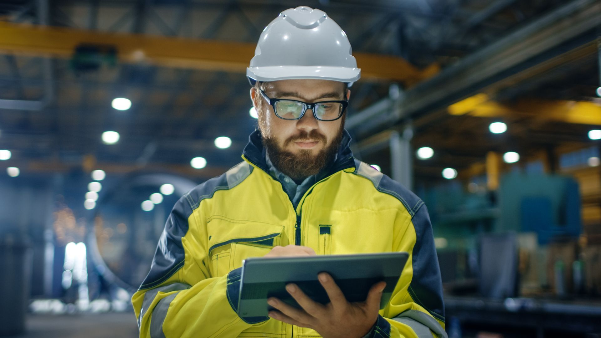 A man in a hard hat is holding a tablet in a factory.