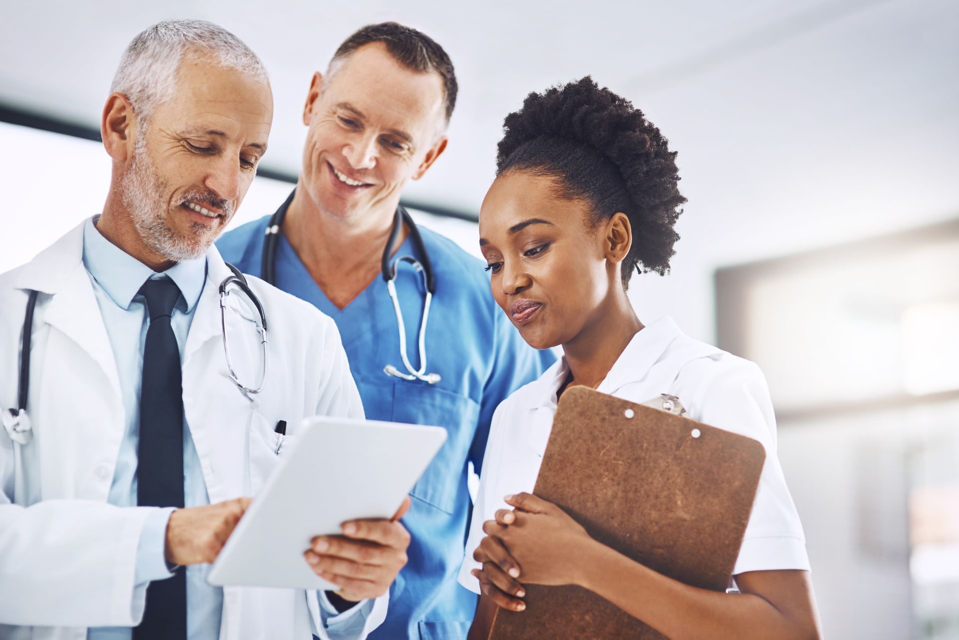 Three medical professionals looking at a tablet and clipboard. 