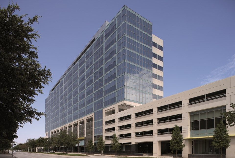 Modern glass-walled office building with attached parking garage against a blue sky.