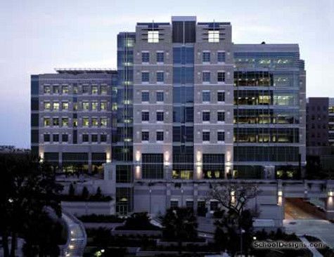 Modern multi-story building with glass and stone facade, exterior lights, dusk setting.